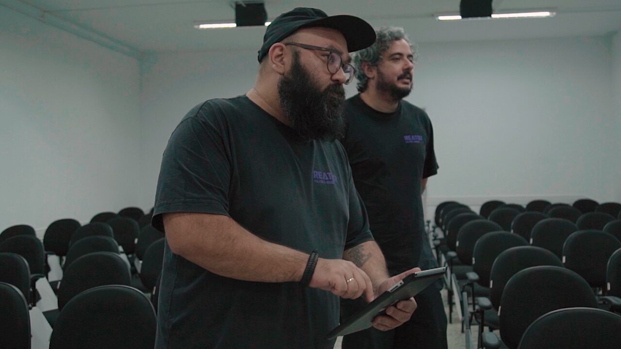 Dois integrantes da Reator, com a camiseta da produtora, preparando uma gravação num auditório